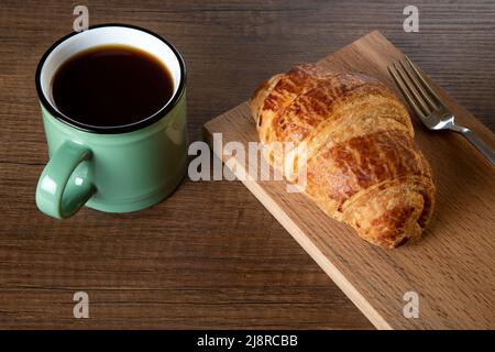 Tasse Kaffee und Croissant auf Holzhintergrund Stockfoto