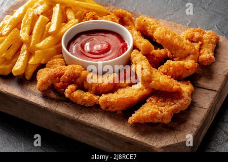 Hähnchendarstellungen, panierte Nuggets, mit einem bbq-Dip und Pommes auf schwarzem Hintergrund Stockfoto