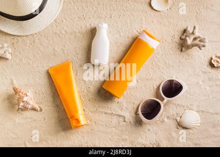 Sommer Reise Strand flach Lay Zusammensetzung. Rattanhut, Sonnenbrille, Sonnenschutzcreme, Sonnenschutzcreme und Muscheln auf Sand am Strand. Sommerurlaub Stockfoto