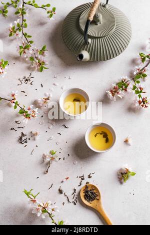 Grüner Tee und Kirschblüte auf weißem Steintisch. Japanische Teekannen aus Gusseisen und Tassen, asiatische Grüntee-Komposition mit Sakura-Blüte und Blütenblättern. Stockfoto