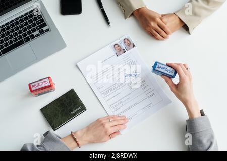 Draufsicht auf Aufnahme eines nicht erkennbaren Konsularbeamten, der nach einem erfolgreichen Interview das Visum für muslimische Frauen genehmigt Stockfoto