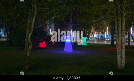 Dekorative, neonleuchtende Pilze auf einem grünen Rasen unter den Bäumen im Nachtpark Stockfoto