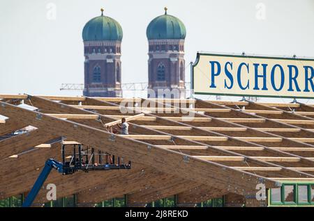 München, Deutschland. 18.. Mai 2022. Auf dem Oktoberfest bauen Arbeiter das erste Bierzelt seit dem Ausbruch der Corona-Pandemie. Das Zelt ist eine komplett neue Konstruktion. Im Hintergrund sind die beiden Türme der Frauenkriche zu sehen. Das Oktoberfest findet in diesem Jahr vom 17. September bis 3. Oktober 2022 statt. Kredit: Peter Kneffel/dpa/Alamy Live Nachrichten Stockfoto