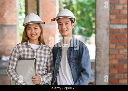 Zwei Bauingenieure mit Schutzhelm stehen auf der Baustelle und lächeln vor der Kamera Stockfoto