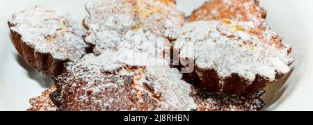 Frisch gebackene Cupcakes auf einem Teller, der mit Puderzucker aus nächster Nähe bestreut wurde. Seitenansicht. Kulinarisches Thema. Stockfoto