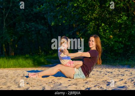 Wunderbare niedliche Baby Mädchen Kind spielt mit glücklichen Mama zwischen grünen Sanddünen Stockfoto