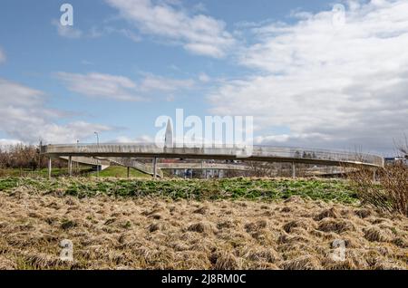 Reykjavik, Island, 25. April 2022: Grasbewachsene Landschaft in der Nähe des Flughafens Vatnsmyri mit einer Fußgängerüberführung und der Ikone Hallgrimskirkja Kirche im Hintergrund Stockfoto