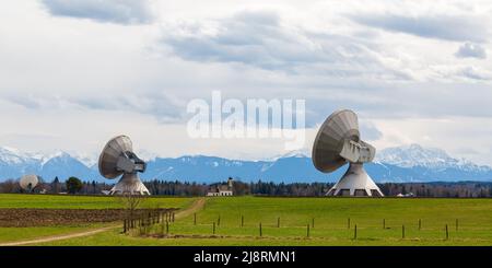 Raisting, Deutschland - 11. Apr 2021: Zwei Satellitenschüsseln des Raisting-Radoms, die in Richtung Himmel zeigen. In der Mitte eine Kirche. Stockfoto
