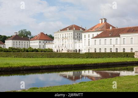 München, Deutschland - 2. Jul 2021: Blick auf das Hauptgebäude des Schlosses Nymphenburg. Wiese und Parkwasser im Vordergrund. Stockfoto