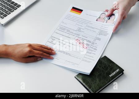 Nahaufnahme eines nicht erkennbaren Konsularbeamten, der der Frau ein Visum-Antragsformular mit abgelehnter Stempelabstempelung zurückgab Stockfoto