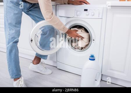 Beschnittene Ansicht des afroamerikanischen Mannes, der Kleidung in die Waschmaschine legt Stockfoto
