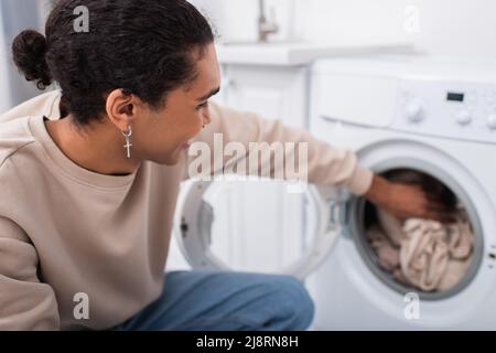Glücklicher afroamerikanischer Mann, der Kleidung in die Waschmaschine legt Stockfoto