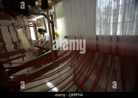 Eine Arbeiterin wird im Vordergrund von Songket-Garnen fotografiert, während sie im Erika Rianti-Songket-Studio in Bukittinggi, West Sumatra, Indonesien, ein Songket-Gewebe produziert. Stockfoto