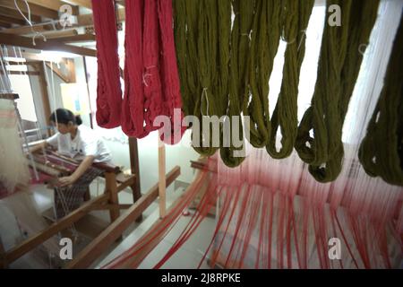 Eine Arbeiterin wird im Vordergrund von Songket-Garnen fotografiert, während sie im Erika Rianti-Songket-Studio in Bukittinggi, West Sumatra, Indonesien, ein Songket-Gewebe produziert. Stockfoto