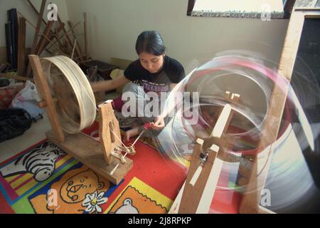 Eine Frau, die Songket-Garne im Erika Rianti-Songket-Studio in Bukittinggi, West Sumatra, Indonesien, rollt. Stockfoto