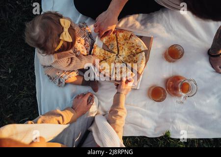 Draufsicht auf die junge Familie Mama Papa und Tochter, die im Freien Picknick machen und Pizza essen Stockfoto