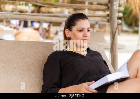 latina Frau liest am Strand Stockfoto