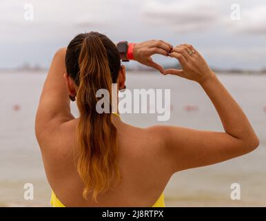 Rückansicht einer Frau am Strand, die mit ihren Händen ein Herzzeichen macht Stockfoto