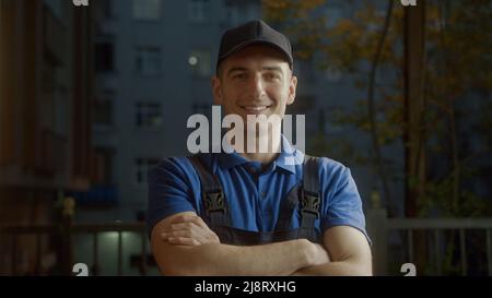 Attraktiver junger Lieferer in blauer Mütze Legen Sie Ihre Hände zusammen und lächeln Sie in die Kamera. Berufskonzept. Stockfoto