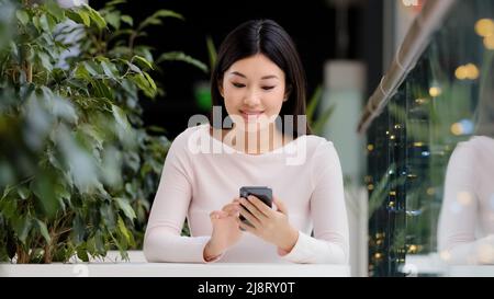 Asiatisch koreanisch Mädchen Benutzer Freiberufler Spieler Frau sitzt im Café am Tisch im Büro mit Telefon jubeln Sieg Sieg gewinnen mobile Spiel succ feiern Stockfoto