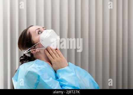 Arzt, der Covid-19 N95-Maske auf ihrem Gesicht in der Aufnahmestelle vor dem Patientenbesuch anpasst Stockfoto