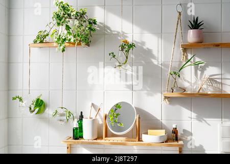 Weiße Fliesenwand mit wönigen Regalen und Kommoden und grünen Pflanzen darauf. Biophile kreative Gestaltung des Badezimmers. Wohnanlage. Zero Waste Konzept Stockfoto