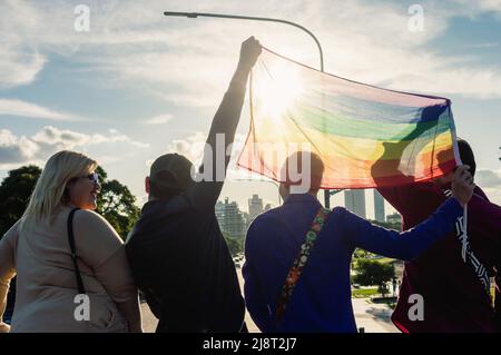 Rückansicht einer Gruppe von Freundinnen und Freundinnen, im Freien mit einer Gay-Pride-Flagge, mit der Sonne, die durch die Flagge scheint, mit Panoramablick auf Th Stockfoto