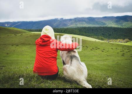 Hikerin, die mit Hund im Freien in der Natur der Berge sitzt. Person Streichelhund. Junges Mädchen verbringt Zeit mit Hund in der Freizeit Stockfoto