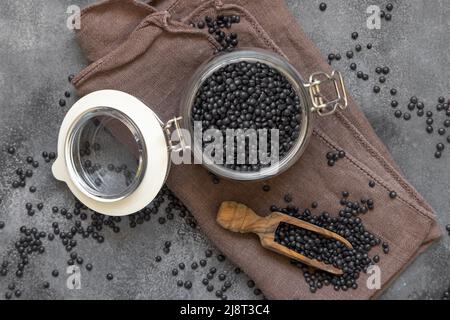 Glas aus trockenen schwarzen Linsen mit einer Holzlöffel auf der grauen Tischansicht. Gesunde Ernährung, Proteinquelle für vegane und vegetarische Ernährung. Tradi Stockfoto