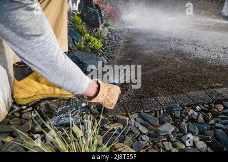 Landschaftsbauarbeiter, der Gartenwassersprinkler in einem neu erbauten Wohnhinterhofgarten anpasst. Moderne Bewässerungssysteme. Gartenarbeit und Landschaftsbau Stockfoto