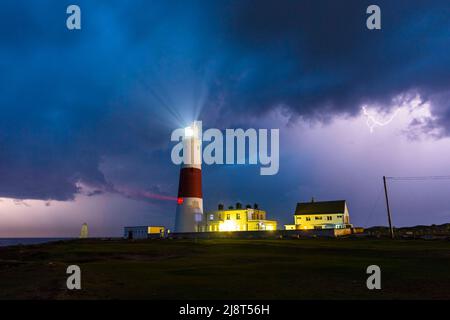Blitze eines vorbeiziehenden Gewitters erleuchten die Wolken am Nachthimmel über dem Leuchtturm von Portland Bill in Dorset. Bild: Graham Stockfoto