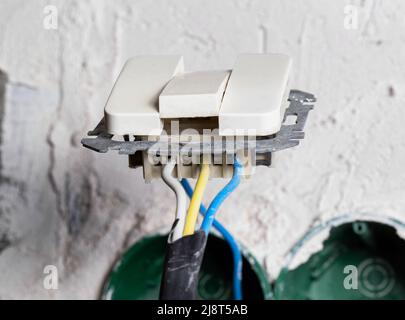 Ein unsicherer elektrischer Schalter hängt an den Kabeln. Elektrische Sicherheit Stockfoto