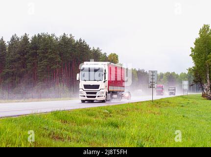 Sattelschlepper, der mit anderen Autos bei starkem Regen im Sommer auf der Autobahn fährt, nasse Straße. Verkehr auf der Straße, halten Sie die Entfernung Stockfoto