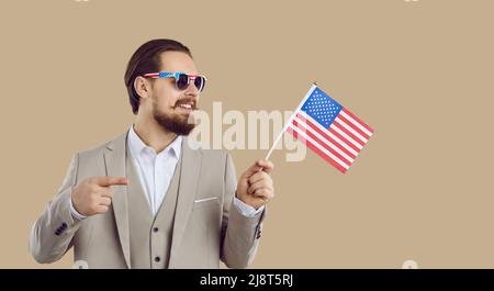 Patriotischer eleganter Mann mit amerikanischer Flagge und Sonnenbrille auf beigem Hintergrund isoliert. Stockfoto