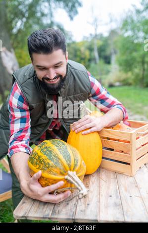 Ein dunkelhaariger junger Bauer mit Kürbissen, die zufrieden aussehen Stockfoto