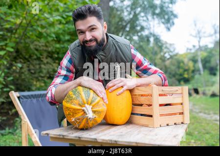 Ein dunkelhaariger junger Bauer mit Kürbissen, die zufrieden aussehen Stockfoto