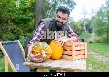 Ein dunkelhaariger junger Bauer mit Kürbissen, die zufrieden aussehen Stockfoto