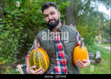 Ein dunkelhaariger junger Bauer mit Kürbissen, die zufrieden aussehen Stockfoto