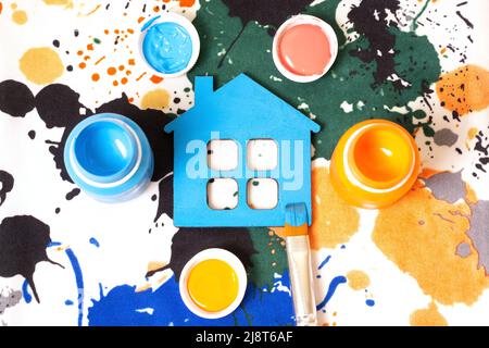 Frisch bemaltes flaches blaues Haus mit Farbflaschen und einem Pinsel auf einem gefärbten Aquarell-Stoff-Hintergrund. Innenrenovierung und Erfrischungskonzept. Stockfoto