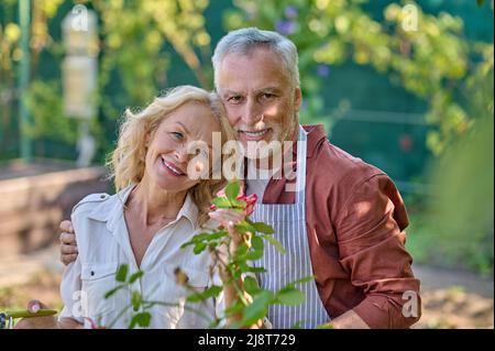 Mann umarmt Frau lächelnd auf Kamera im Garten Stockfoto