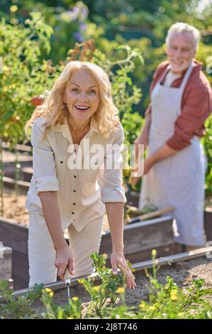 Frau lächelt auf die Kamera, die in der Nähe des Gemüsegartens arbeitet Stockfoto