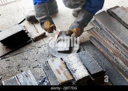 Arbeiter in der Schwerindustrie oder Metallurgie schlagen Eisenplatten mit Hammer ab. Arbeiten Sie mit Metall. Beschaffung von Wertstoffen für die Produktion. Authentischer Workflow. Stockfoto