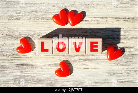 WORTLIEBE aus hölzernen Buchstabenblöcken, eingerahmt von roten Herzen auf einem hölzernen Hintergrund. Stockfoto
