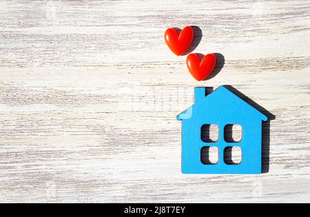 Flache blaue Hausform mit zwei kleinen roten Herzen auf einem Holztisch mit Kopierfläche. Stockfoto