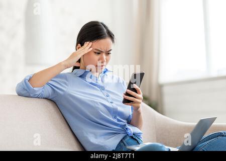 Verwirrt asiatische Geschäftsfrau mit Laptop und Smartphone zu Hause Stockfoto