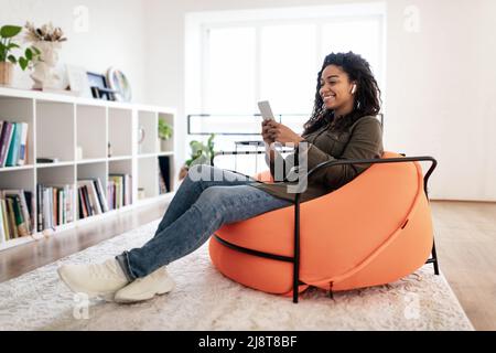 Lächelnde schwarze Frau mit schnurlosem Kopf und Mobiltelefon Stockfoto