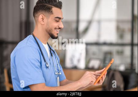 Fokussierter, fröhlicher Arzt tippt auf sein Gadget Stockfoto