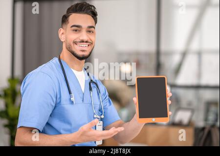 Glücklicher junger Arzt, der seine Tablette vorführt Stockfoto