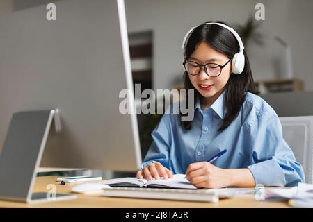Frau, die am Schreibtisch saß, Computer benutzte und im Notebook schrieb Stockfoto