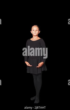 Junges Mädchen in tanzenden Kleidern steht in Position vor schwarzem Hintergrund Stockfoto